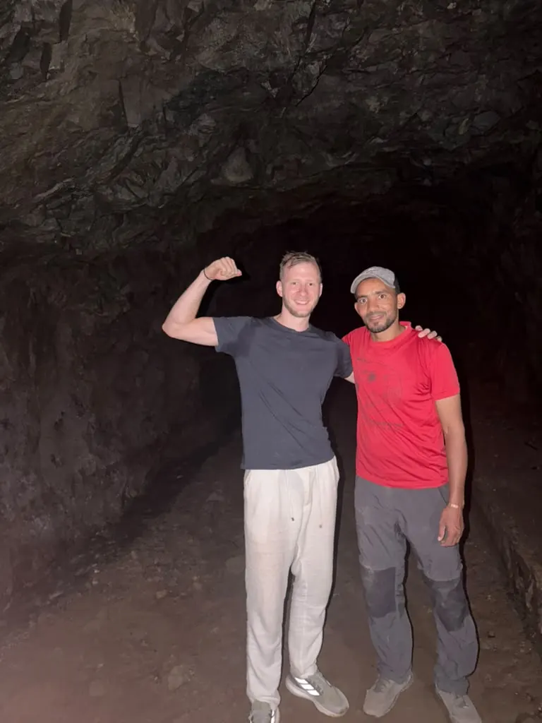 Khalid and a guest flexing their arms inside a dark mountain cave