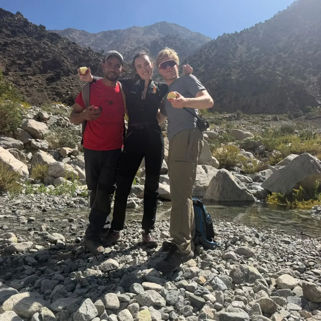 Khalid with two guests eating apples on a dry riverbed