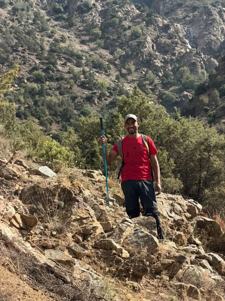 Khalid, a local Berber guide in a red shirt, smiling with his trekking pole in the High Atlas