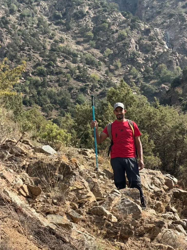 Khalid in his red shirt holding a trekking pole on a mountain trail
