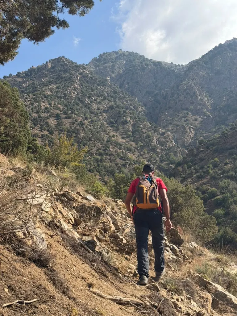 Khalid seen from behind with an orange backpack, walking a mountain trail