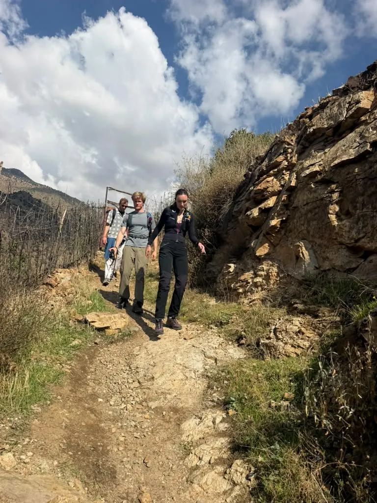 Three hikers in trail shoes walking down a rocky dirt path in the Ourika Valley under a blue sky