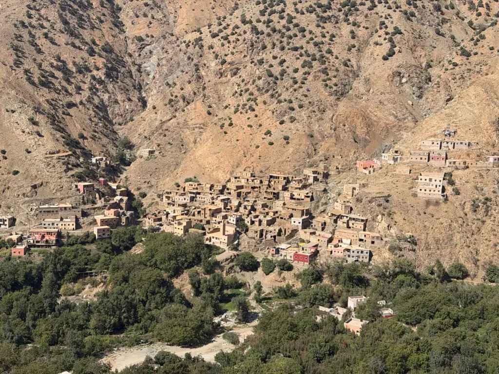 An earthen Berber village on a dry mountainside above green orchards